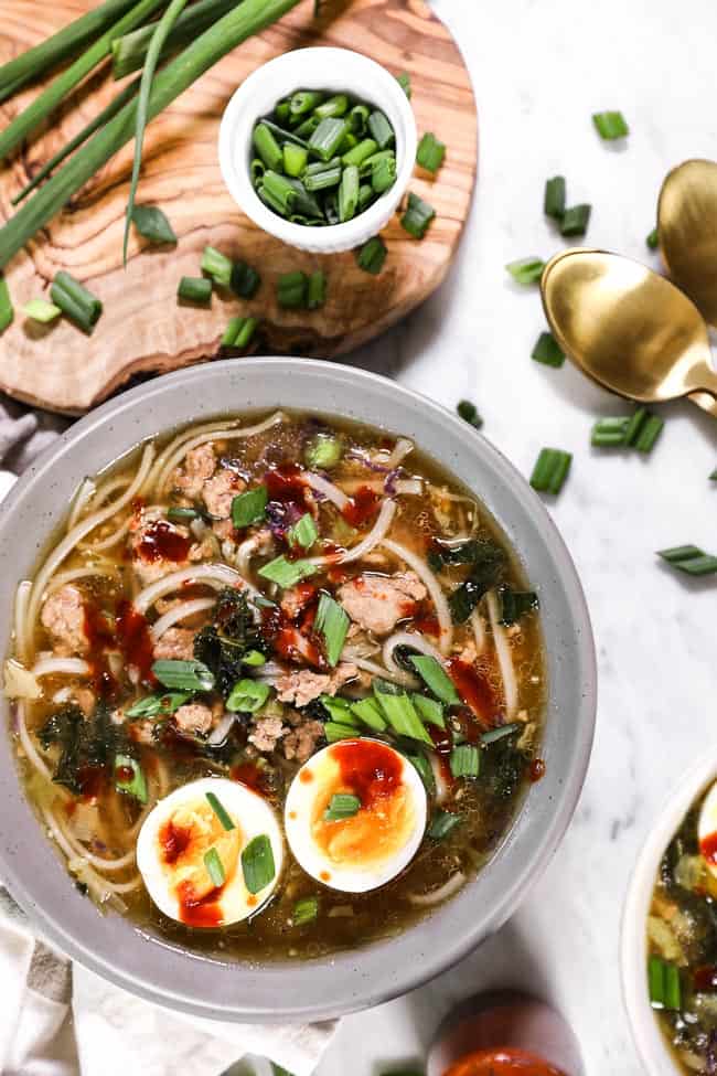 Bowl of pork ramen noodles, topped with chopped green onion, a soft boiled egg and hot sauce. 