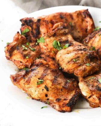 Angled image of a plate of grilled chicken thighs with chopped cilantro sprinkled on top.