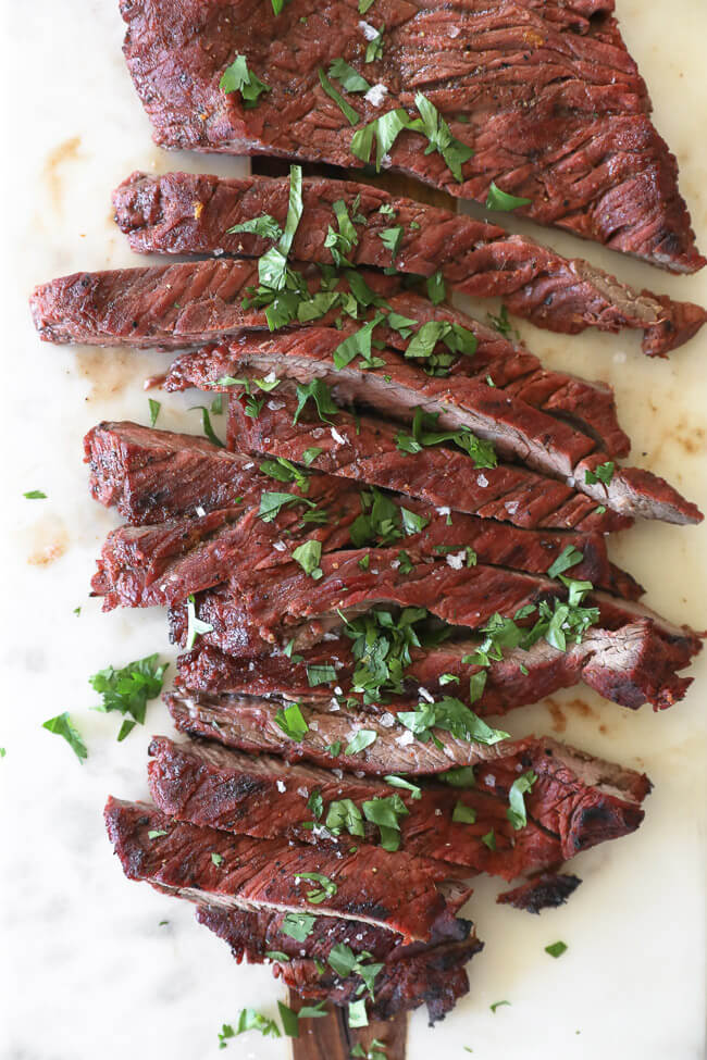 Carne asada steak on a board cut into strips topped with salt and cilantro overhead vertical image