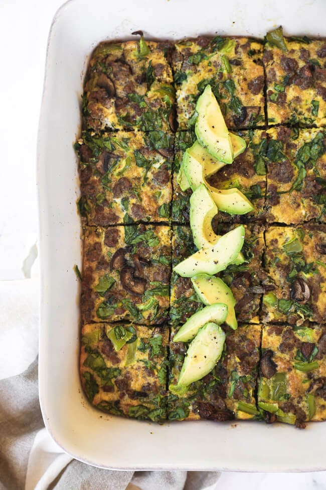 Keto breakfast casserole sliced in a dish with sliced avocado topping overhead vertical image