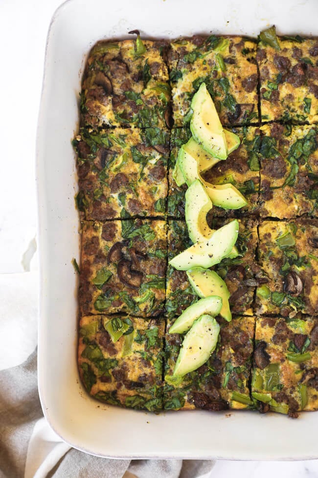 Keto ontbijt ovenschotel gesneden in een schaal met gesneden avocado topping overhead verticale afbeelding