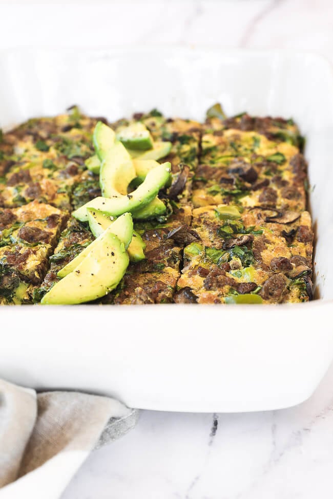 Keto breakfast casserole sliced in a dish with sliced avocado close up angle image