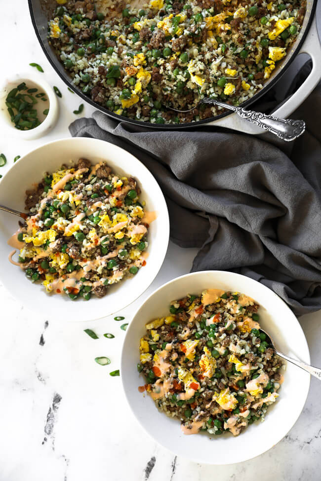 Overhead shot of two bowls filled with cauliflower fried rice and sauce drizzled on top