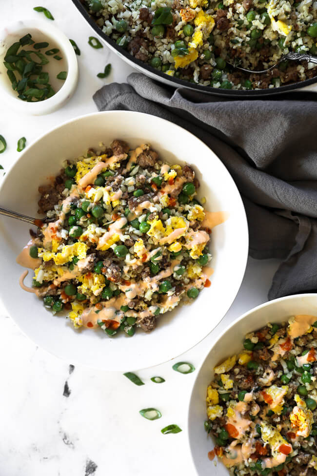 Overhead image of keto pork fried rice in a white bowl with spoon and sauce drizzled on