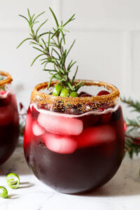 Close up straight on shot of red iced drink with brown sugar rim and rosemary sprig garnish