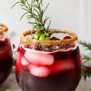 Close up straight on shot of red iced drink with brown sugar rim and rosemary sprig garnish