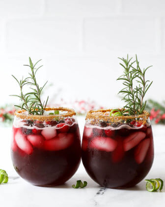 Straight on shot of two red christmas gin cocktails with rosemary sprigs sticking out