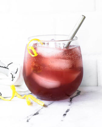 Straight on vertical image of a pink vodka lemonade cocktail with lemon peel garnish