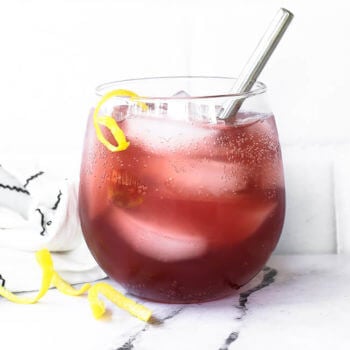 Straight on vertical image of a pink vodka lemonade cocktail with lemon peel garnish