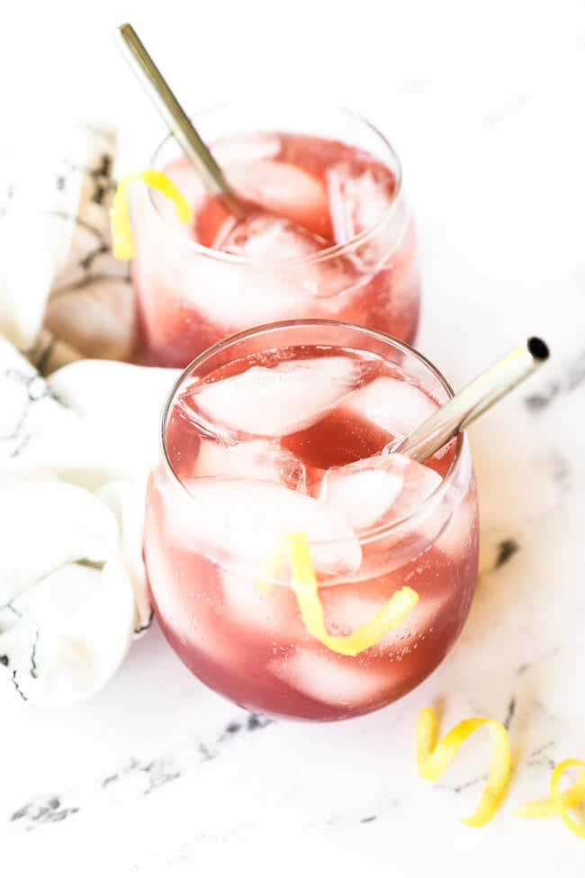 Angled image of this refreshing cocktail in a glass with a stainless steel straw and lemon rind garnish. Second glass in the background. 