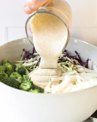 Image of pouring creamy sauce into bowl with keto coleslaw ingredients.