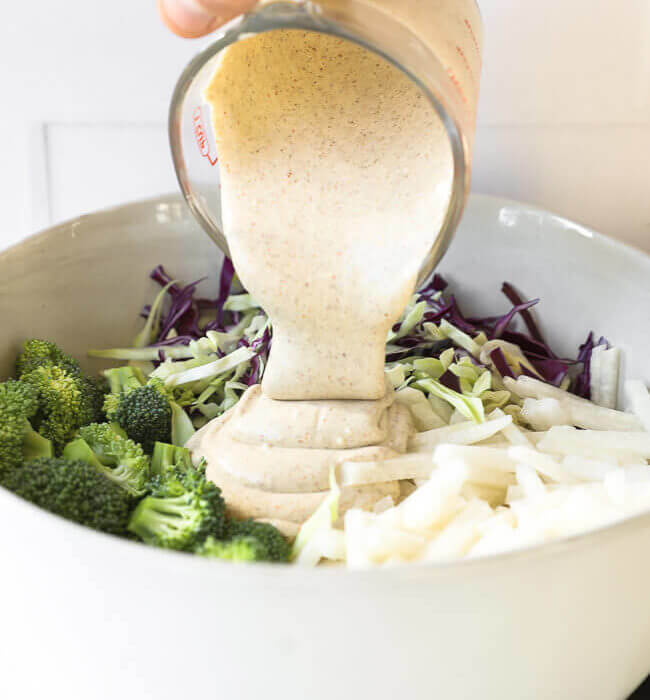 Image of pouring creamy sauce into bowl with keto coleslaw ingredients.