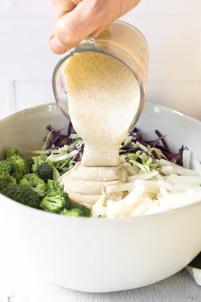 Image of pouring the creamy sauce into bowl with the rest of the low carb coleslaw ingredients. 