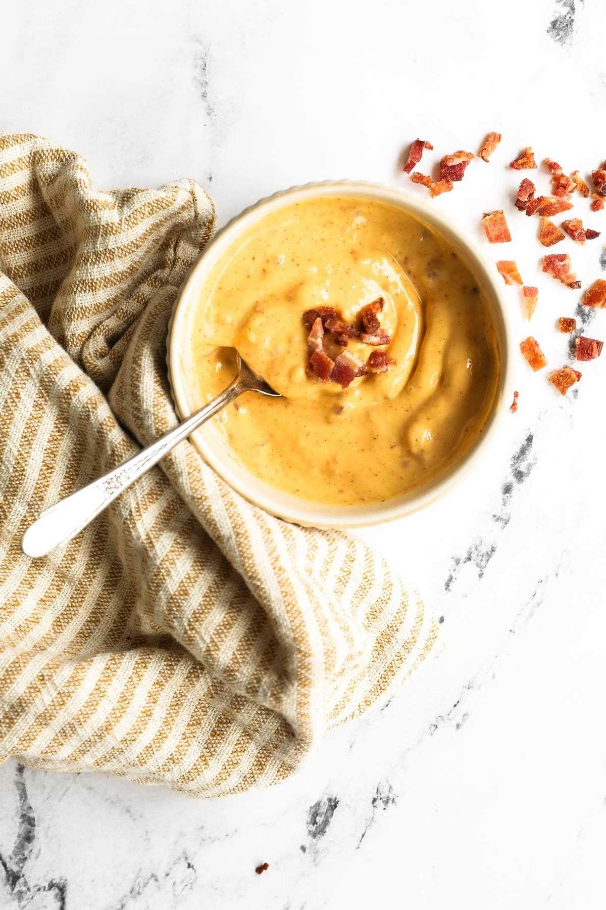 Overhead shot of bacon aioli in a ramekin with spoon and bacon pieces on the top and side