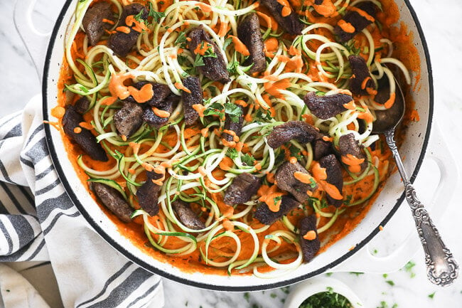 zoodles and orange sauce with steak bits in a pan