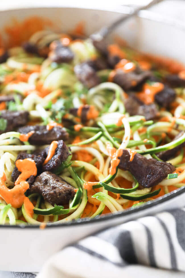 Close up angle of zoodles and orange sauce with steak bits in a pan
