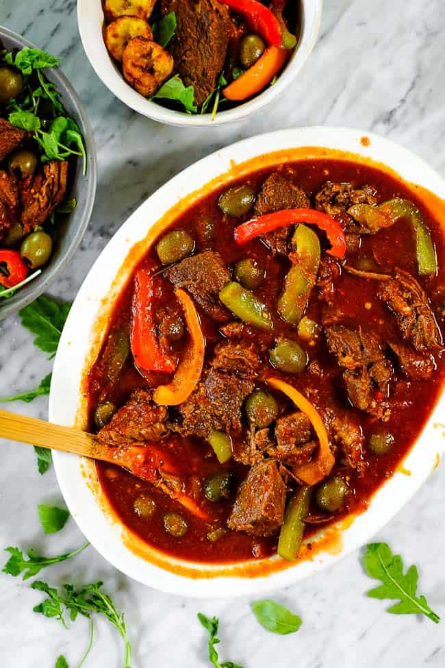 Ropa vieja in a large serving dish with a spoon and served in bowls on the side. 