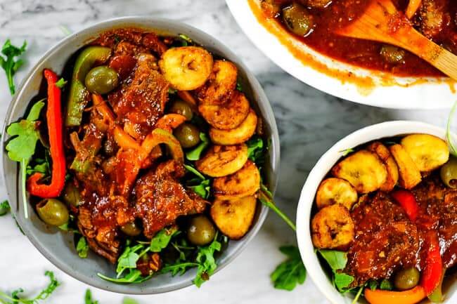 Ropa vieja served in bowls with greens and fried plantains. 