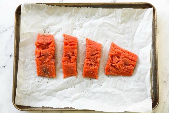 Raw salmon pieces on a sheet pan with salt and pepper