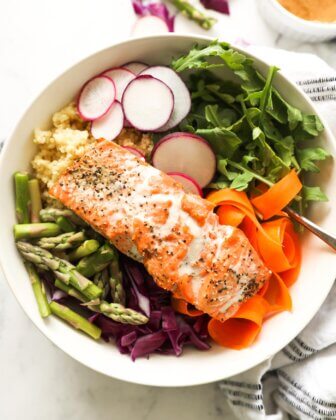 Close up overhead image of salmon buddha bowls over radish, arugula, millet, carrot, cabbage and asparagus