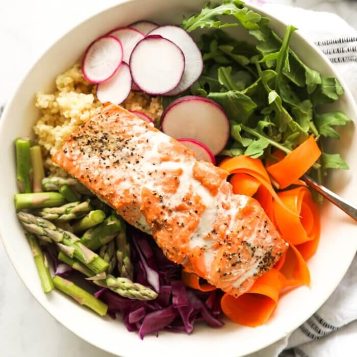 Close up overhead image of salmon buddha bowls over radish, arugula, millet, carrot, cabbage and asparagus
