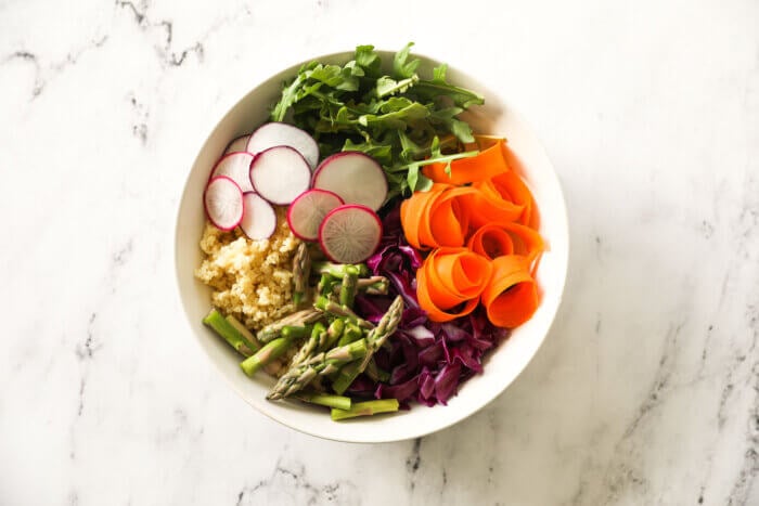 Carrots, cabbage, asparagus, millet, radish and arugula separated out in a bowl.