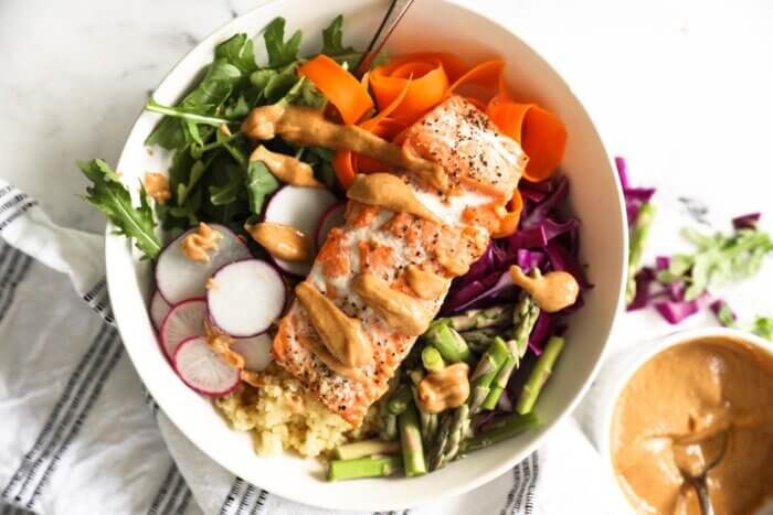 Cooked salmon buddha bowl with peanut sauce drizzled over the top