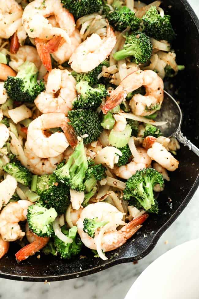 Image of seafood stir-fry cast iron skillet with serving spoon in pan. Stir fry has shrimp, white fish, broccoli, celery and onion and cajun seasoning. 