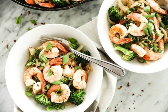 Image of seafood stir-fry served in two bowls, with shrimp, white fish, broccoli, celery and onion and cajun seasoning. Topped with chopped green onion and red pepper flakes. 