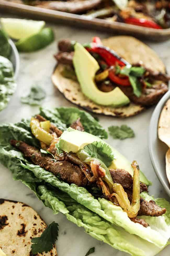 Angled image of sheet pan fajitas in romaine lettuce leaves with avocado and cilantro on top. 