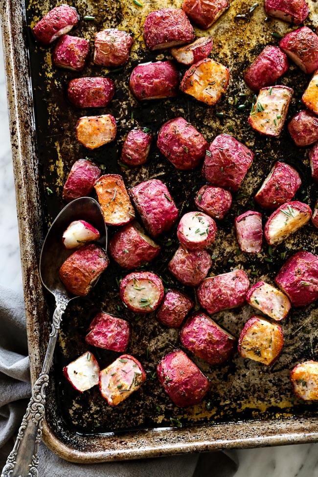 Roasted radishes on sheet pan with spoon overhead vertical image