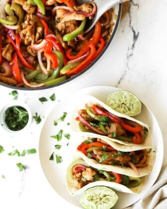 3 Skillet chicken fajita tacos on a plate with lime wedges and skillet on the side