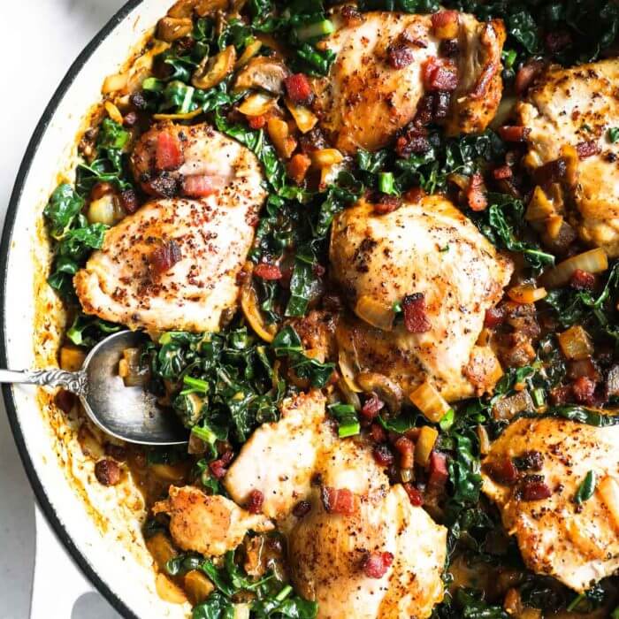 Overhead image of skillet chicken thighs in mustard sauce with kale and bacon