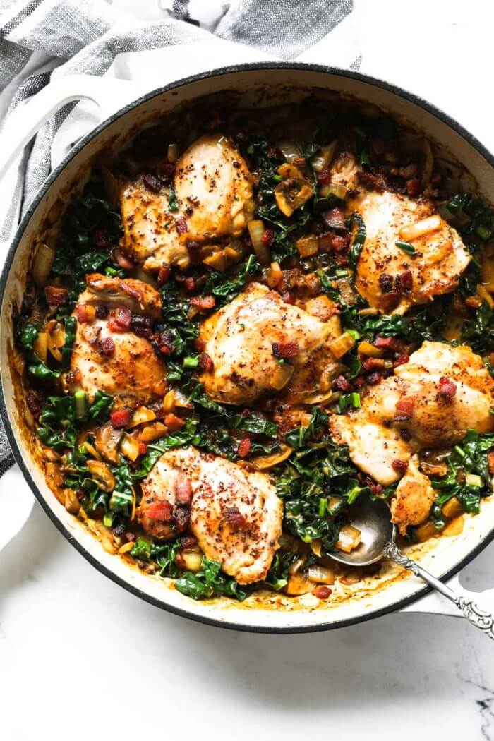 Overhead image of cooked chicken thighs with kale, mushrooms and bacon with a spoon coming out