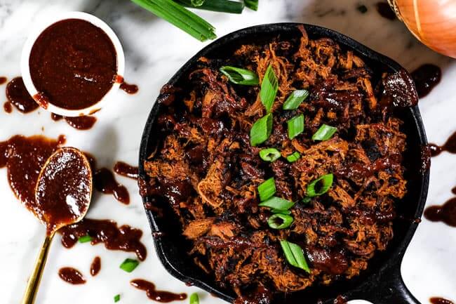 Slow cooker BBQ beef in cast iron skillet after re-heated and topped with extra BBQ sauce and chopped green onion. Extra sauce and messy spoon on the side. 