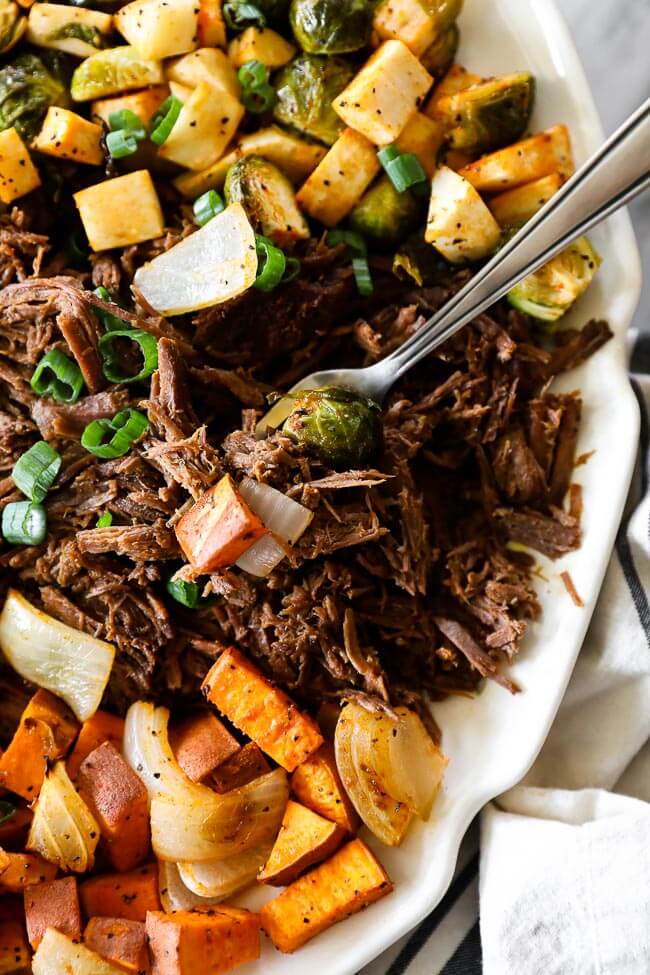 Close up overhead shot of slow cooker beef pot roast on platter with fork on side