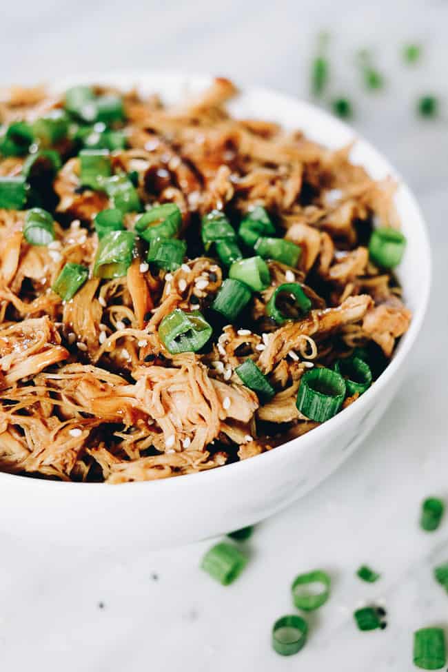 Slow cooker teriyaki chicken in a bowl with green onion and sesame seeds
