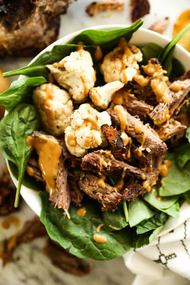 Pulled smoked chuck roast in a bowl with greens and cauliflower with mustard sauce over top 