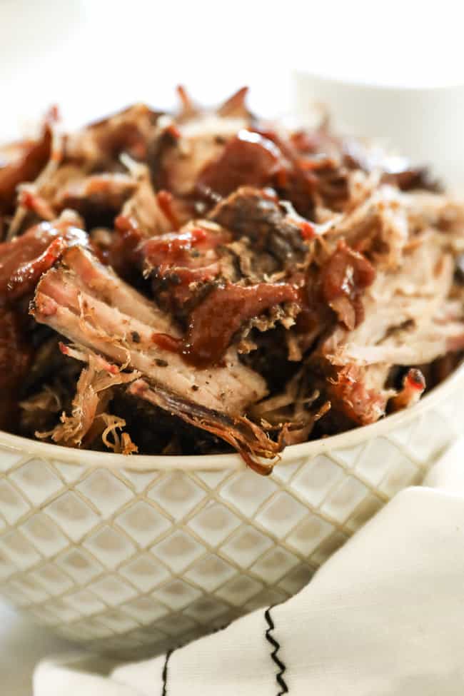 Smoked pork shoulder pieces in a bowl with sauce over the top angle close up shot