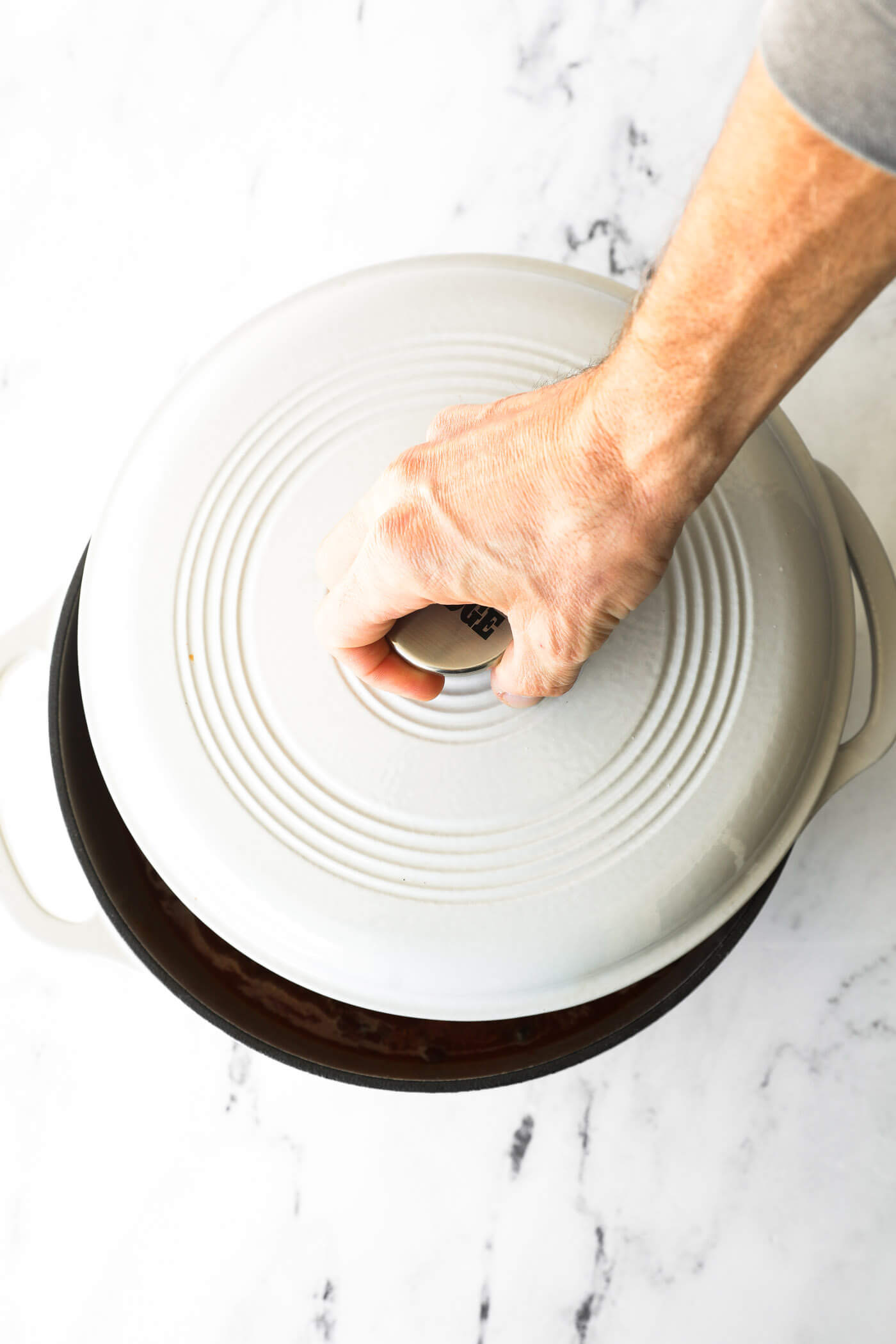 A hand putting the cover on the dutch oven with a lid to simmer the chili on the stove. 