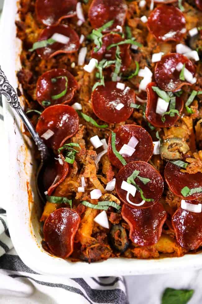 Close up overhead shot of spaghetti pizza casserole in casserole dish. Topped with fresh chopped red onion and basil. 