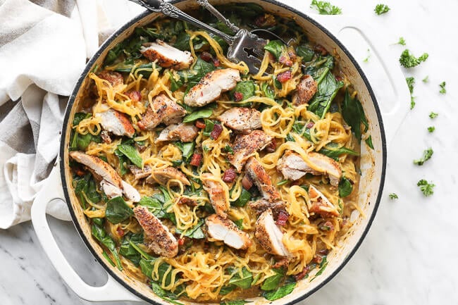 Horizontal overhead image of spaghetti squash carbonara in a skillet with a serving fork and spoon dug in. 