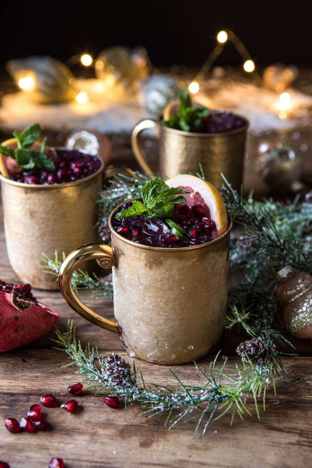 3 Pomegranate moscow mules in copper cups with christmas decorations around them