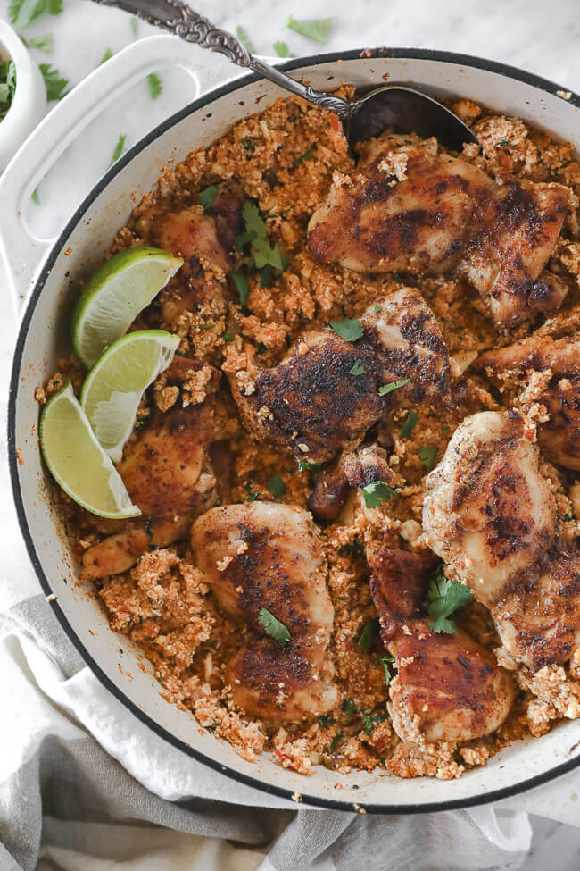 Spicy chicken thighs and cauliflower rice in pan with lime wedges close up overhead vertical shot