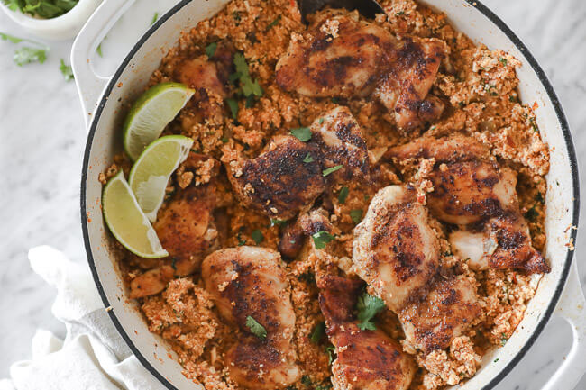 Blackened chicken thighs and cauliflower rice in pan with lime wedges overhead horizontal shot