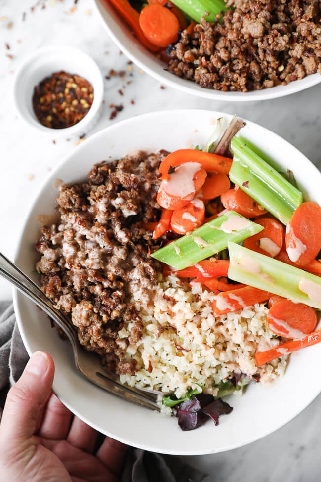 Overhead close up image of holding a bowl of spicy pork, cauliflower rice and veggies. 