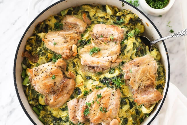 Horizontal image of spinach artichoke chicken in skillet with serving spoon dug in. Topped with chopped parsley. 