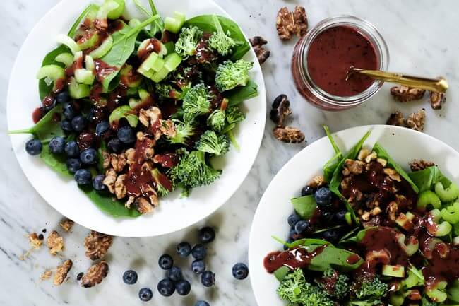 Spinach blueberry salad on plates with extra walnuts and blueberries spread around and blueberry dressing on the side. 