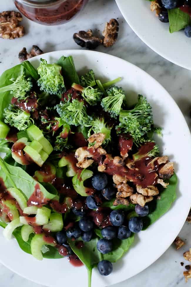 Spinach blueberry salad on plates with extra walnuts and blueberries spread around and blueberry dressing on the side. 