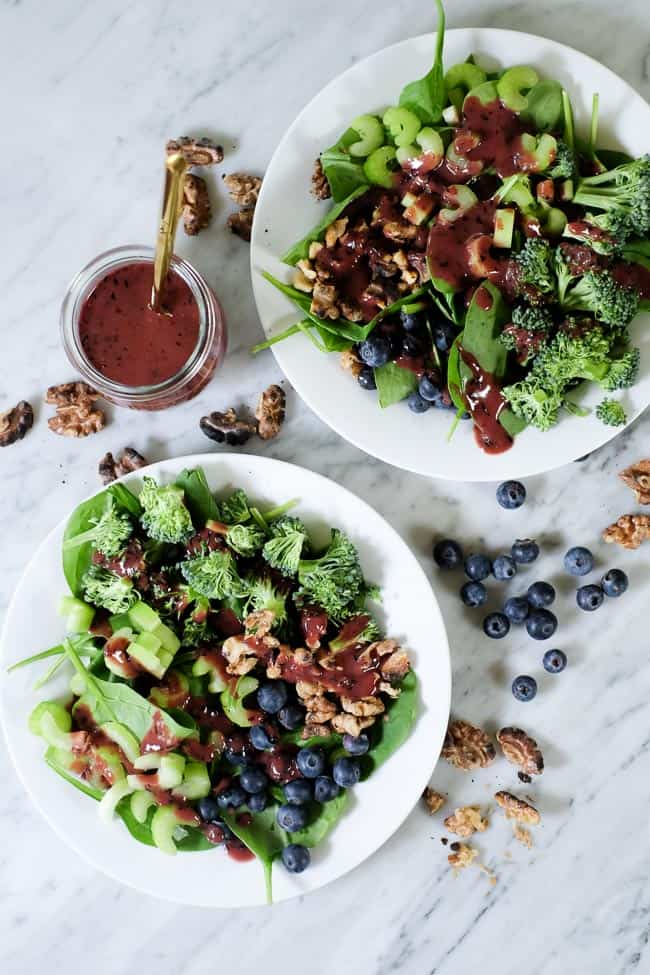Spinach blueberry salad on plates with extra walnuts and blueberries spread around and blueberry dressing on the side. 
